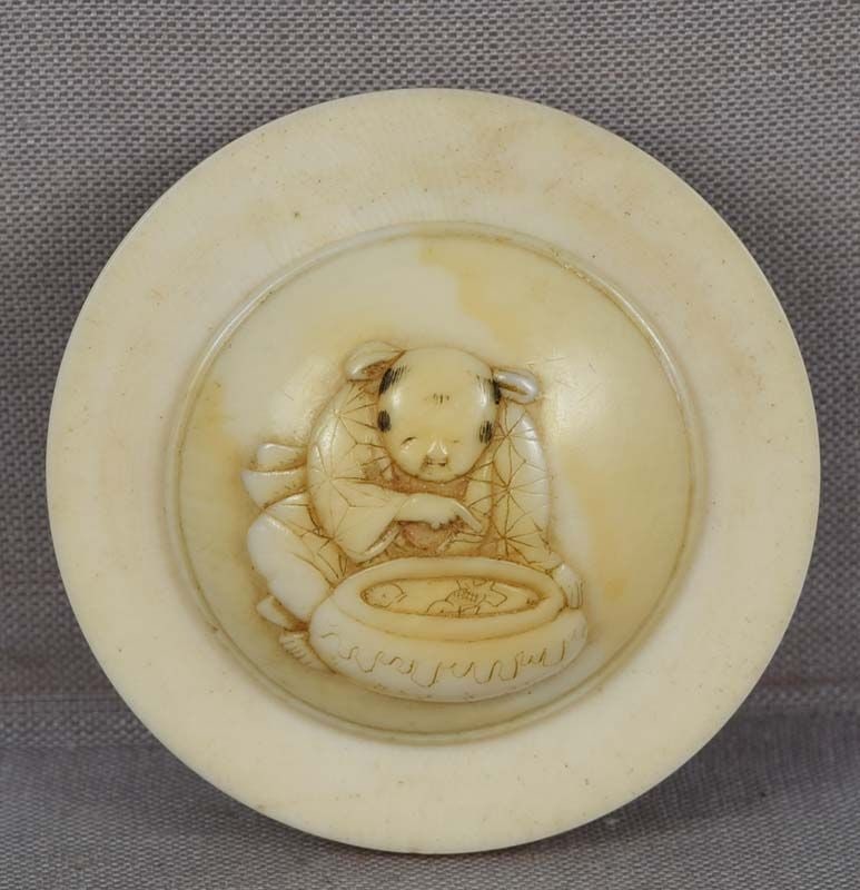 19c kagamibuta netsuke BOY watching fish: 19th century kagamibuta (“mirror lid”) netsuke with the top carved in low relief with a seated boy wearing rich robe decorated with brocade pattern and intently looking at koi fish