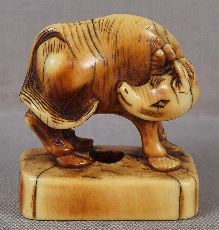 Early 19c netsuke STYLIZED BUFFALO: Early 19th century netsuke of a buffalo on a base, its head turned back. Unusual and wonderful stylization of the creature - see its upturned snout and raised ears and horns. Beautifully carved, excel