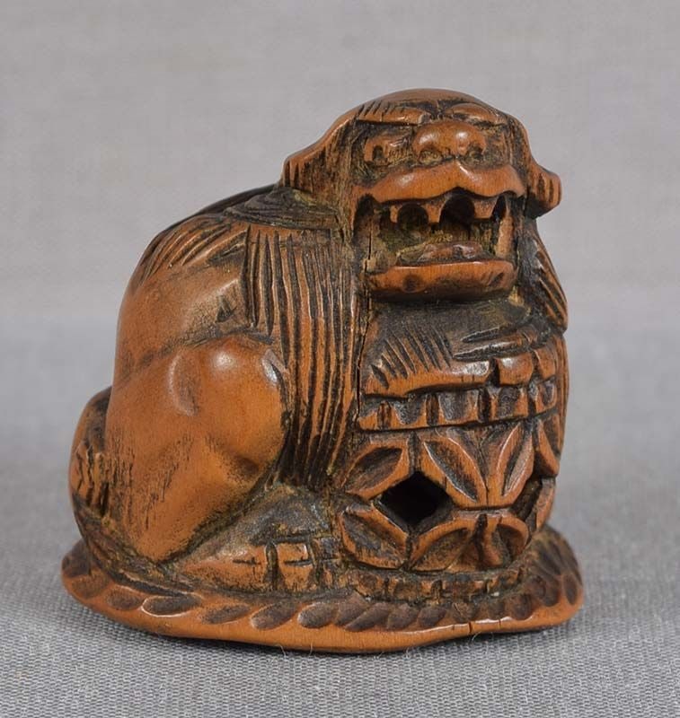 18c netsuke SHISHI with ball: Late 18th to early 19th century boxwood netsuke of a shishi (Buddhist lion) seated with its front paw on a largehollow ball, its mouth open and upper teeth showing. Wonderful depiction of its ferociou