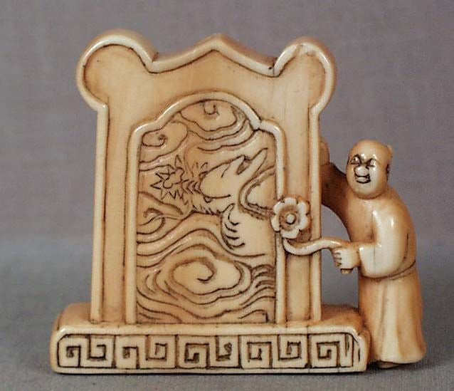 19c netsuke BOY by DRAGON SCREEN ex Mary O’Brien: 19th century netsuke of a karako (Chinese boy) with a flower in his hand standing by a tall floor screen decorated with a dragon in flight among clouds. Very nice carving, beautiful light staining, pl