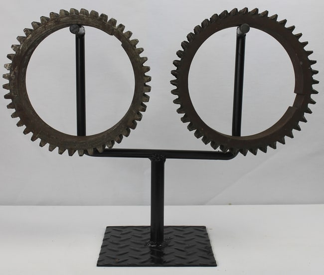 2 large decorative industrial iron gears: These are two large, decorative industrial iron gears with a dark oxidized surface, one slightly darker than the other. There is a massive quality to them. They are mounted on a new metal display