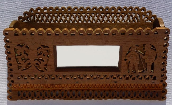 A hand cut fretwork wall box with carved decoration, dated 1927: This is a hand cut fretwork wall box or comb case with carved decoration, dated 1927. The front has two hunters on the right and a floral design on the left, with a mirror set in between the two.
