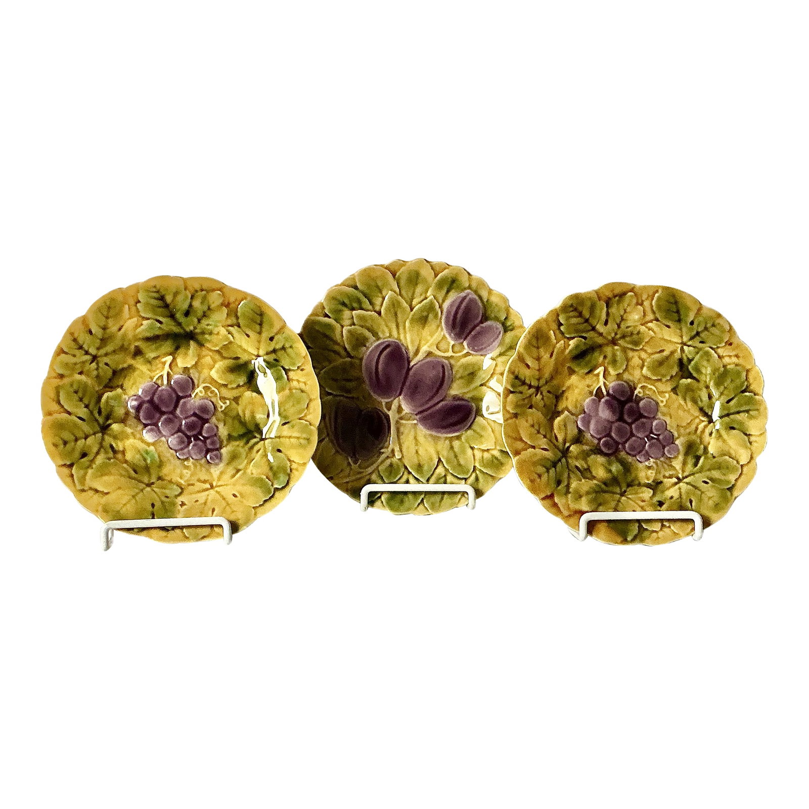 Sarreguemines French Majolica Plates, Set of Three: Early 20th Century Sarregueimines French Majolica Fruit and Leaf Plates, Set of Three. These 7.5" diameter collectible plates feature fruit motifs, two have purple grapes and one has plums, set