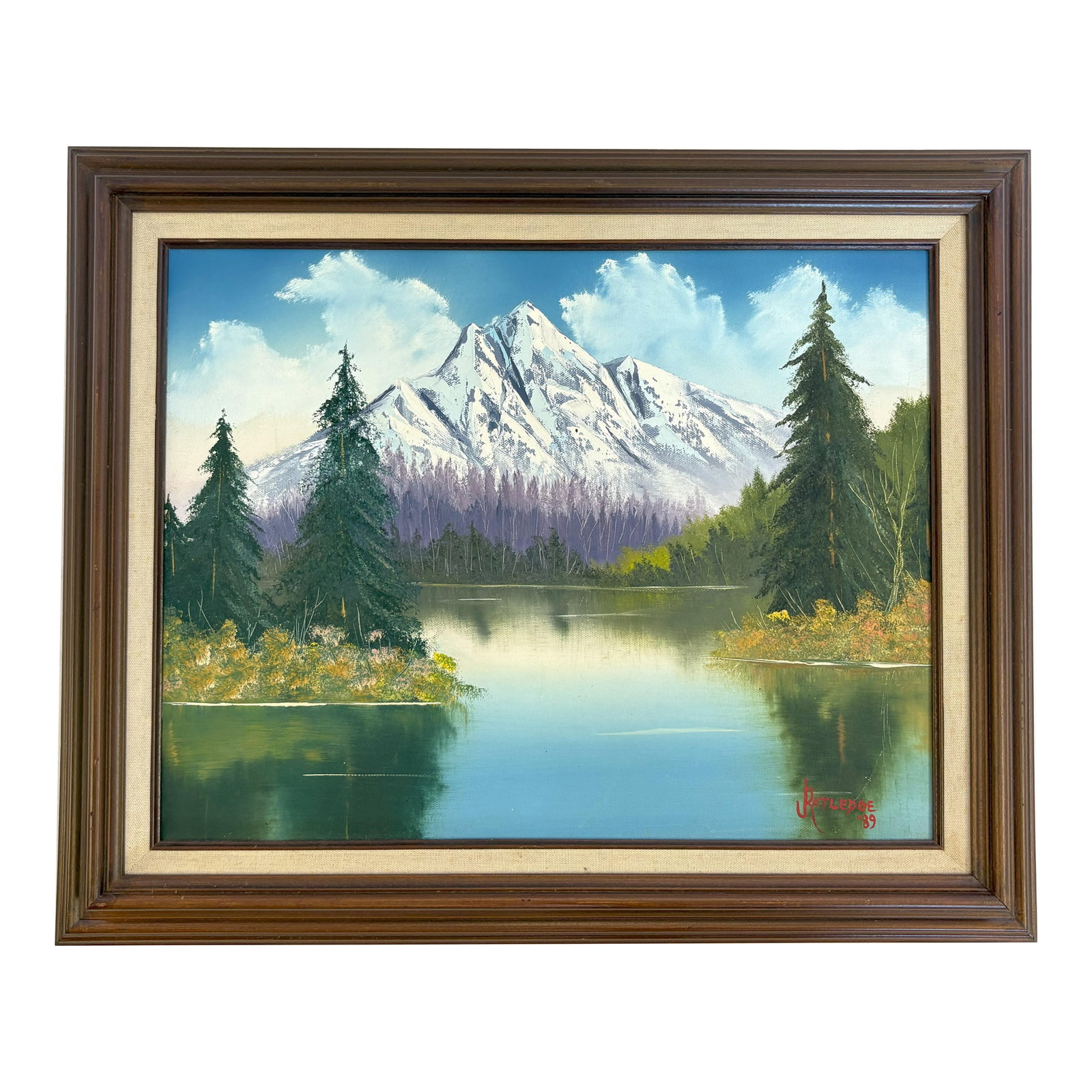 Original Signed and Framed Painting on Canvas by J. Ratledge C1989 'Mountain Landscape': Picturesque original painting on canvas by J. Ratledge circa 1989. The realistic painting depicts a colorful mountain landscape including evergreen trees, a tranquil lake and snowcapped mountains. It