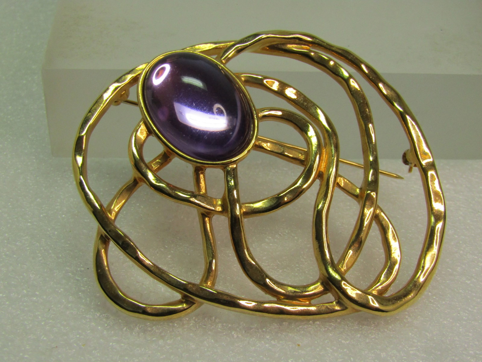 Vintage Large Swirled Brooch, Purple Oval Stone, 1980's-1990's, Mod Design.: Vintage Large Swirled Brooch, Purple Oval Stone, 1980's-1990's. This is gold tone with a hammered type look to the meandering weave of gold tone throughout the 2.75" by 2.25" brooch. I do see this lis