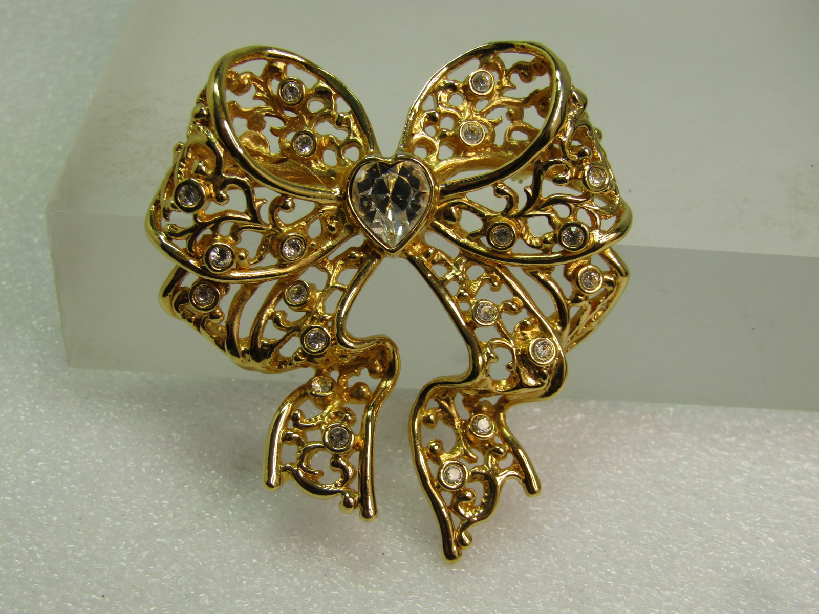 Vintage Rhinestone Heart Filigree Bow Brooch, OSI, Simthsonian, 1980's-1990's: Vintage Rhinestone Heart Filigree Bow Brooch, OSI, Simthsonian, 1980's-1990's. Gold tone with a looped and curved bow with tails and clear rhinestones set throughout and a heart rhinestone at the cent