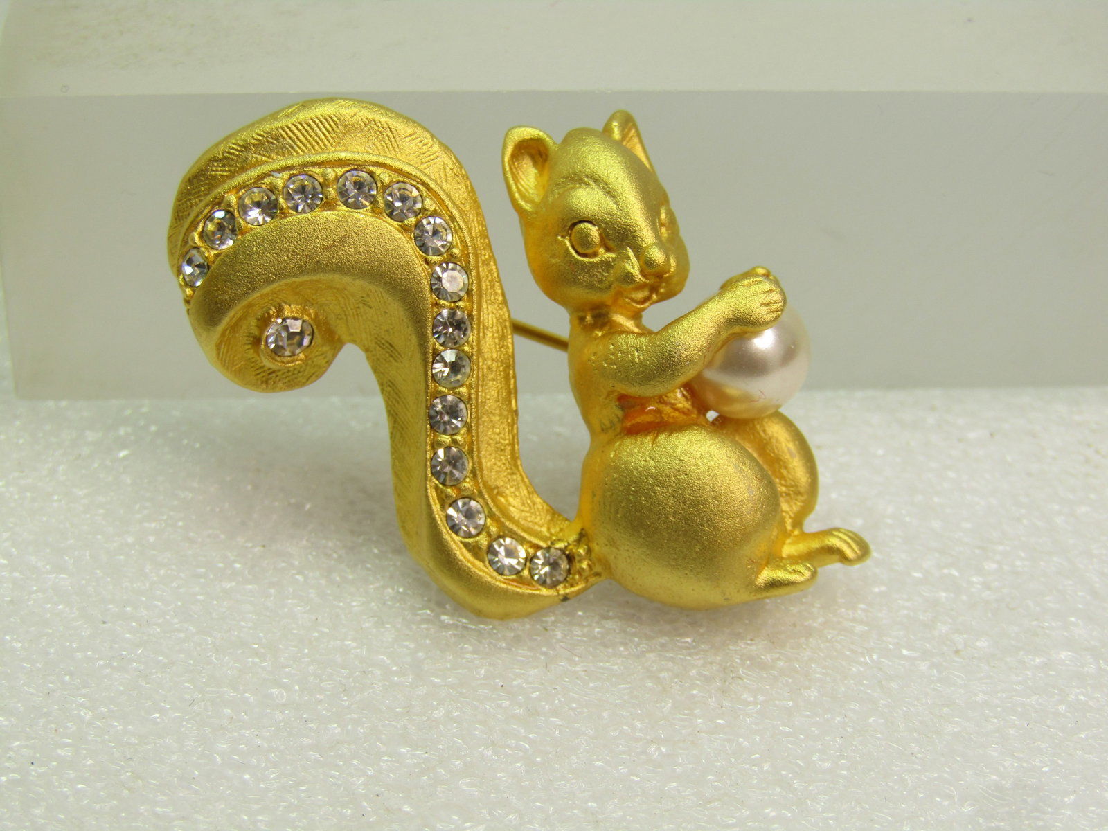 Squirrel Brooch with Faux Pearl Rhinestone Tail, Signed MOD, 2000's: Squirrel Brooch with Faux Pearl Rhinestone Tail, Signed MOD, 2000's. This is a satiny and textured gold tone finish with a sitting squirrel holding an aPpx. 7.5mm white faux pearl and a line of clear