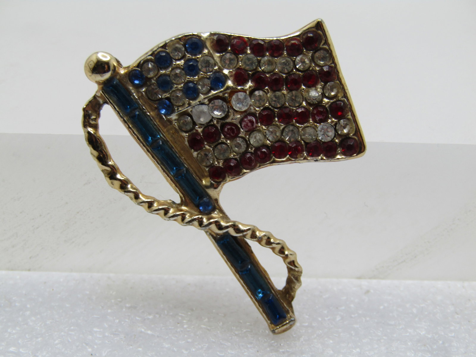 Vintage Red/Clear/Blue USA Flag Brooch 1960's-1970's: Title: Vintage Red/Clear/Blue USA Flag Brooch 1960's-1970's Description: Vintage Red/Clear/Blue USA Flag Brooch 1960's-1970's. Gold tone with a wraping rope around the blue baguette pole with red, cle