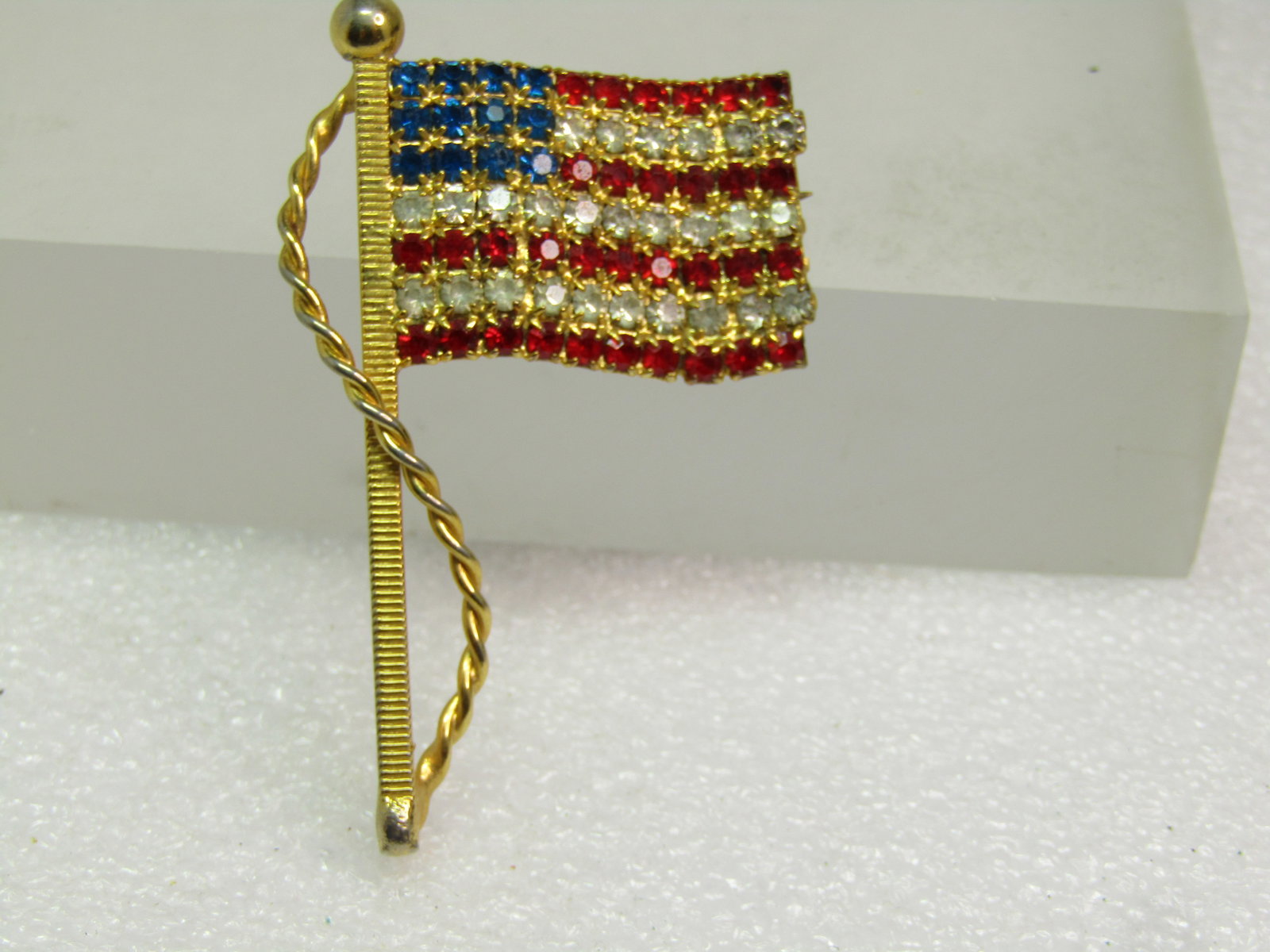 Vintage Rhinestone USA Flag Brooch, 1980's, Red/White/Blue: Title: Vintage Rhinestone USA Flag Brooch, 1980's, Red/White/Blue Description: Vintage Rhinestone USA Flag Brooch, 1980's, Red/White/Blue. Gold tone with a wavy flag design and rope fromt he top of th
