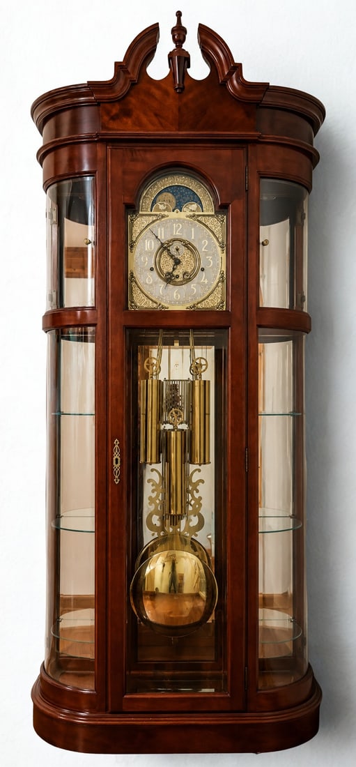 Howard Miller Grandfather Clock with Curio Cabinet, Late 20th Century: A handsome Howard Miller grandfather clock, likely from the late 20th century, crafted from rich cherry-finished wood. The clock features a classical broken pediment top with a finial, and an ornate