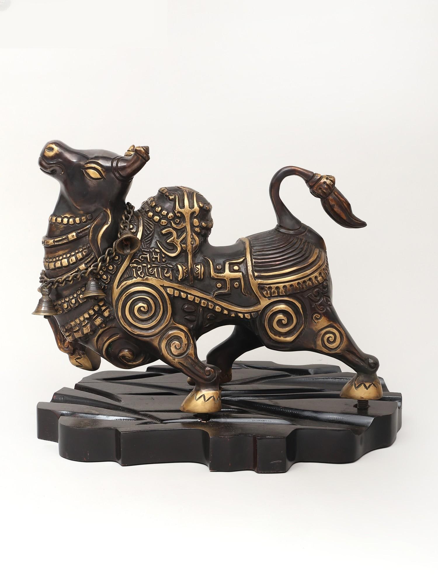 Nandi in Ananda- Bull of Lord Shiva Brass Statue on Wooden Base: Title: Nandi in Ananda- Bull of Lord Shiva Brass Statue on Wooden Base Description: This brass statue of Nandi, mounted on a carved wooden base, captures the bull's sacred presence with a rare combina