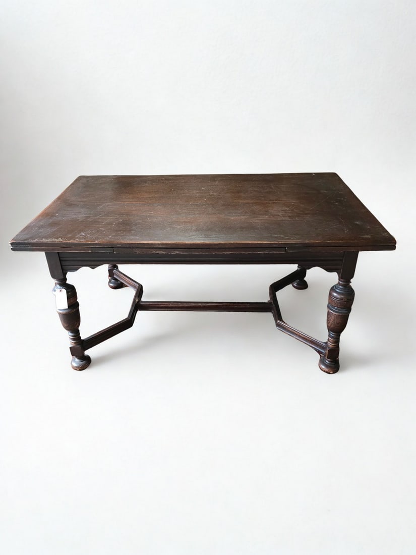 Jacobean Revival Oak Drop Leaf Table: A Jacobean Revival style oak drop leaf table, likely early 20th century. This rectangular table features a plank top with a rich, dark finish, supported by a stretcher base with carved baluster and