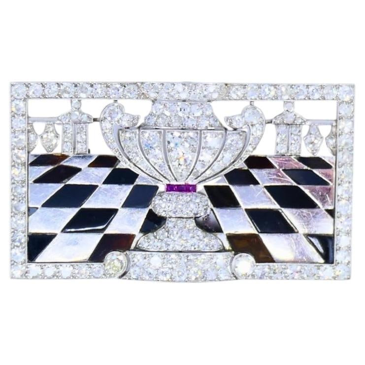 Art Deco Platinum Diamond Brooch Black Onyx Ruby 1920s Vintage Jewelry: A striking Art Deco platinum and diamond brooch, featuring black onyx and ruby; circa 1920s. The brooch’s centerpiece features a trophy-like vase set with old European and single-cut diamonds, a
