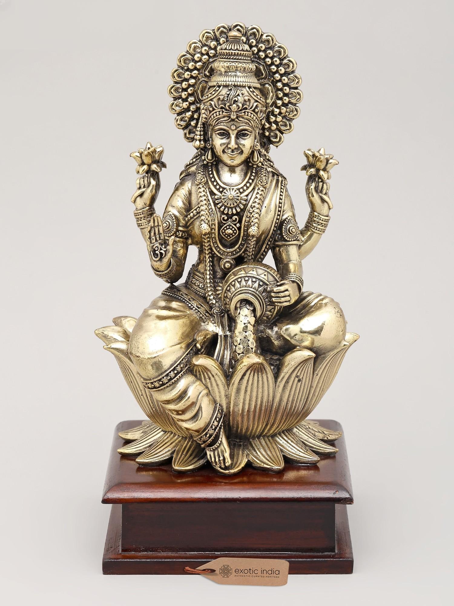 Superfine Goddess Lakshmi Seated on Lotus Flower with Wood Base | Brass Idol | Made in India: Embodiment of Prosperity and Grace: The Goddess Lakshmi This exquisite brass statue captures the divine essence of Goddess Lakshmi, the Hindu deity of wealth, prosperity, fortune, and beauty. Seated