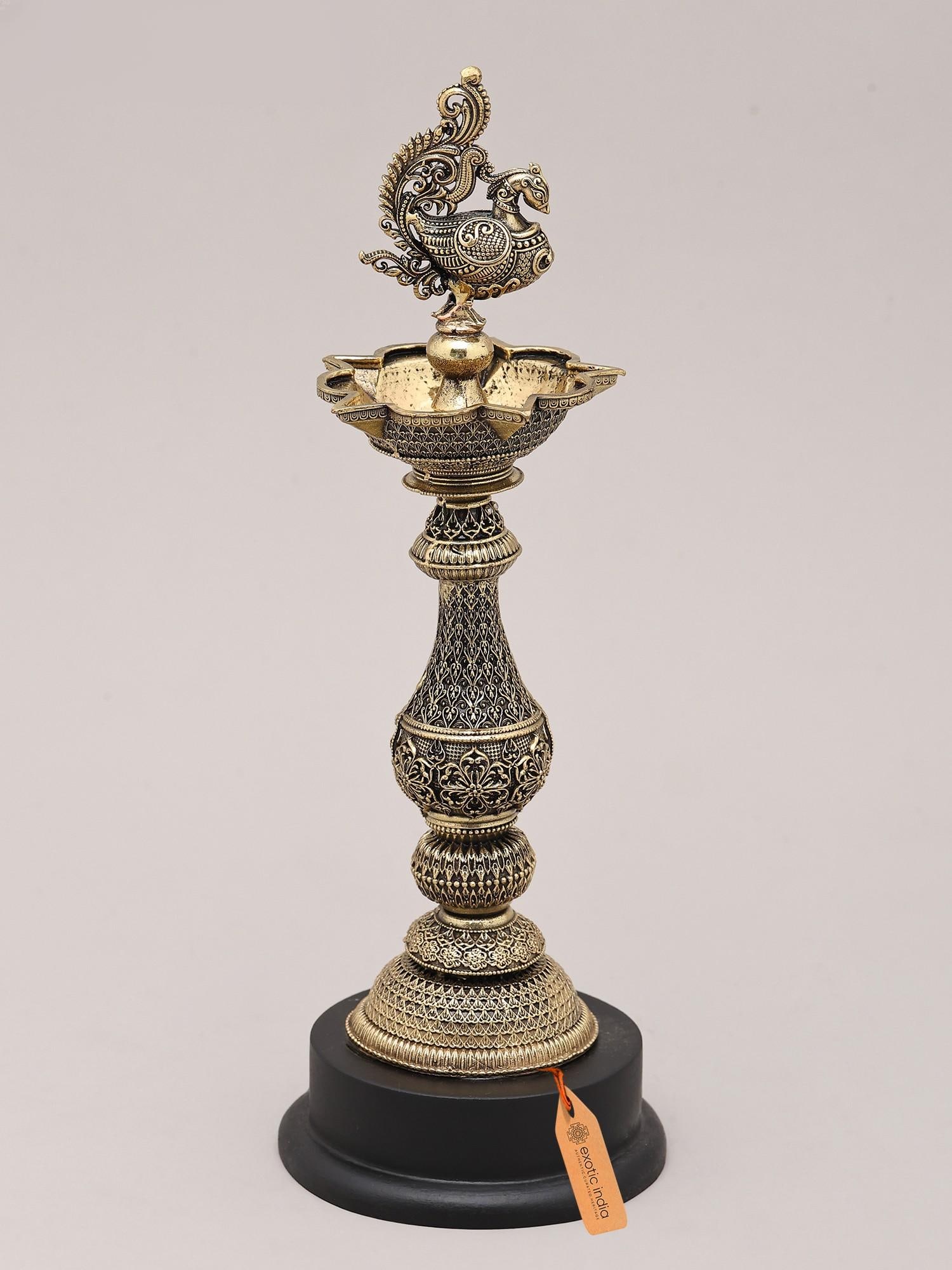 9" Peacock Brass Oil Lamp with Wood Base for Home and Temple | Made in India: The Peacock's Radiant Glow: An Emblem of Auspiciousness This exquisite brass oil lamp, adorned with a majestic peacock, is a testament to the rich artistic heritage of India. More than just a source o