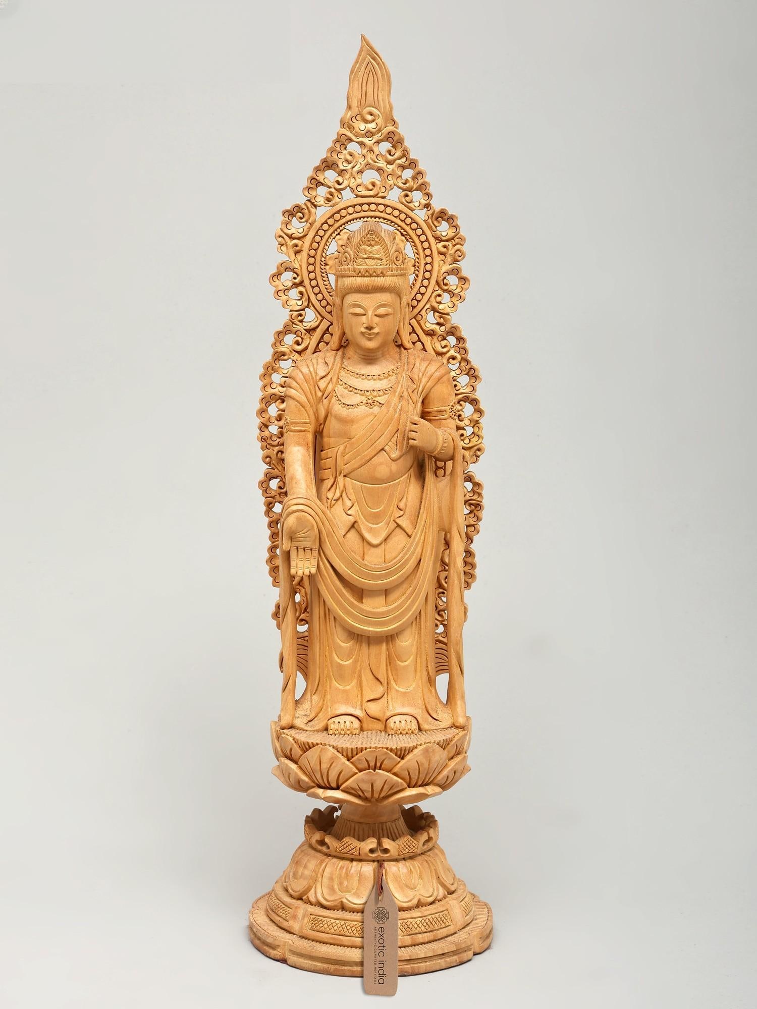 18" Lord Buddha Standing in Varada Mudra on Lotus Pedestal | Wood Carved Statue: Embrace Serenity with a Masterpiece of Divine Craftsmanship This exquisite wooden statue captures the essence of profound peace and compassionate presence. Crafted from fine wood, the figure stands