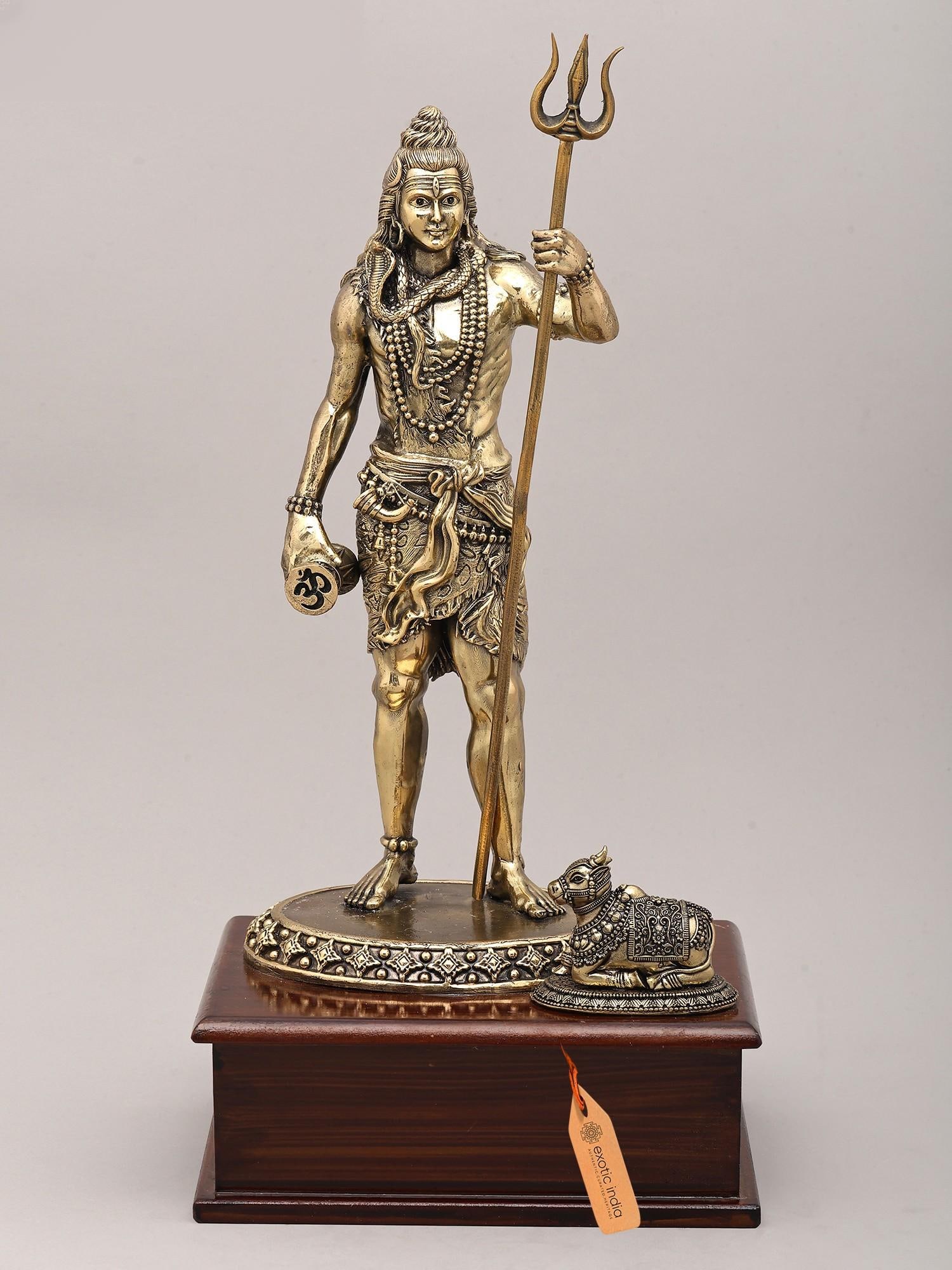 13" Superfine Standing Gesture Lord Shiva with Damaru, Trident and Seated Nandi on Wood Base | Brass: The Ascetic Lord: A Timeless Brass Representation of Mahadeva This exquisite brass statue captures the essence of Lord Shiva, the destroyer and transformer, in a poised standing posture. Crafted with 