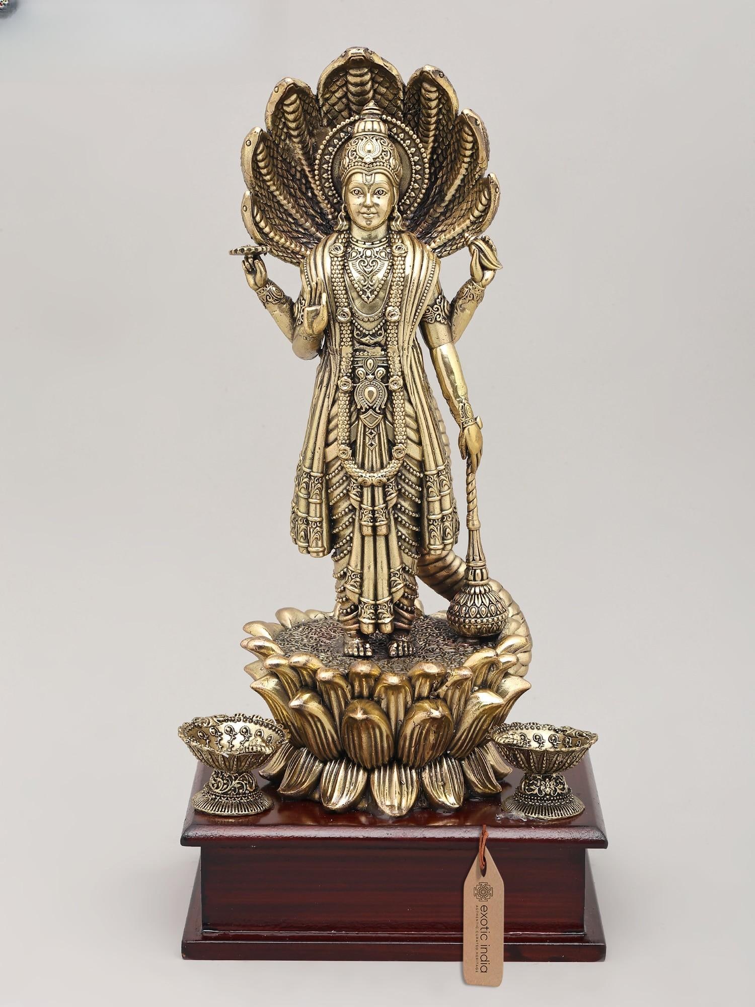 12" Superfine Four Armed Lord Vishnu with Seven Headed Sheshnag and Wood Base | Brass Idol: The Divine Protector and Cosmic Serpent This magnificent brass idol captures the essence of Lord Vishnu, the preserver and protector of the universe, in a moment of profound cosmic significance. Stand