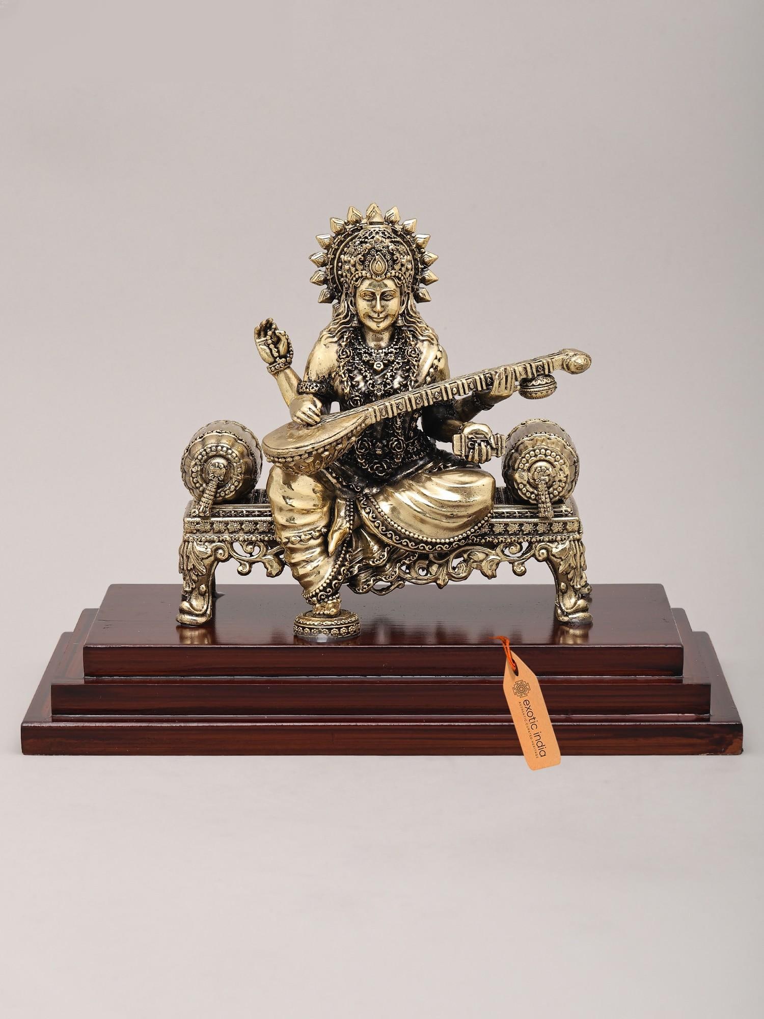 9" Superfine Goddess Saraswati Seated on Asana and Playing Sitar with Wood Base | Brass Idol: The Divine Melody of Knowledge and Art This exquisite brass idol captures the very essence of Goddess Saraswati, the divine patroness of knowledge, music, art, wisdom, and learning. Seated gracefully