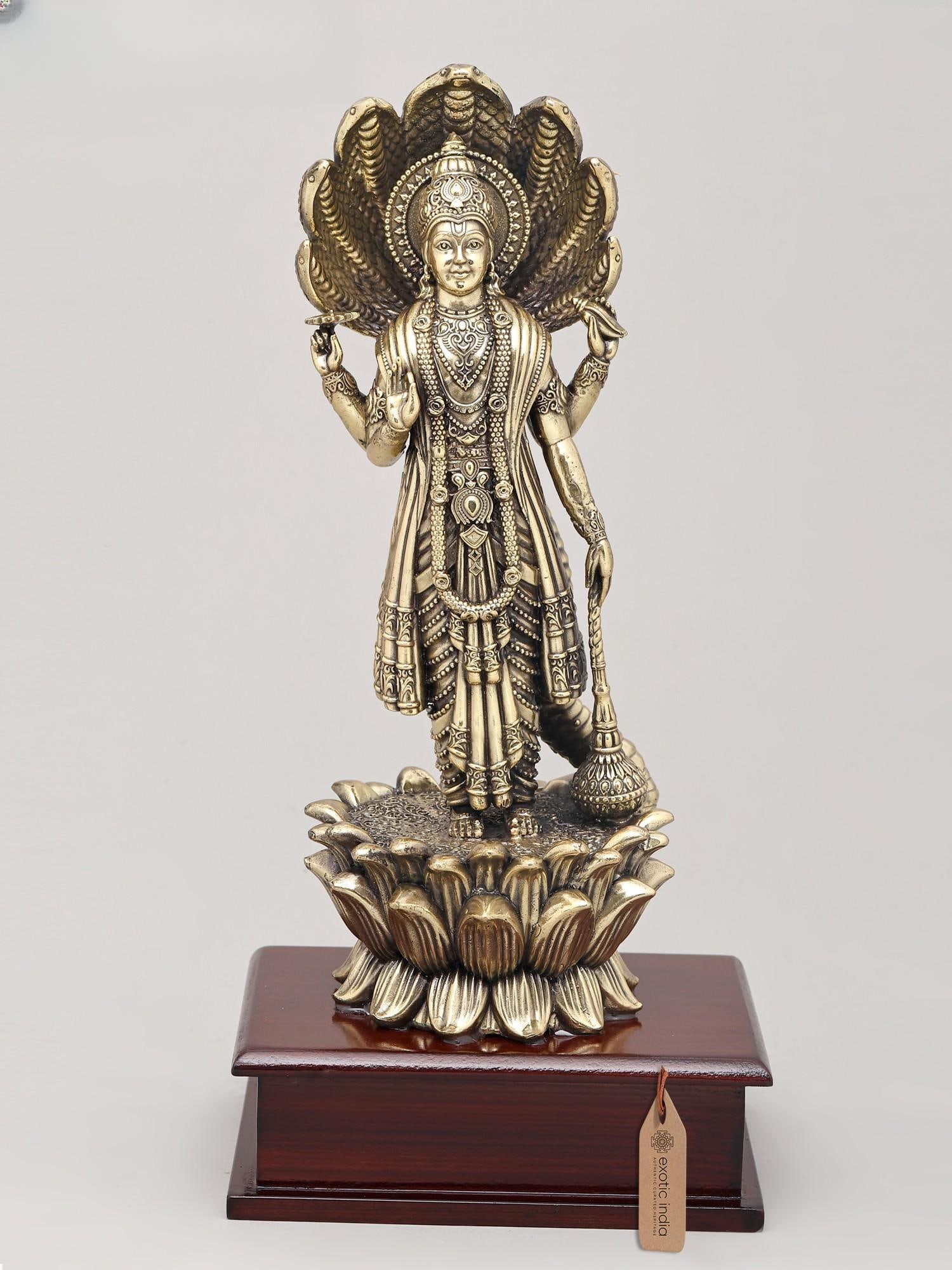 12" Superfine Lord Vishnu Standing on Lotus with Sheshnag Canopy with Wood Base | Brass Sculpture: The Divine Presence of Lord Vishnu This exquisite brass sculpture captures the serene majesty of Lord Vishnu, the preserver of the universe in Hindu mythology. Standing atop a beautifully rendered lot