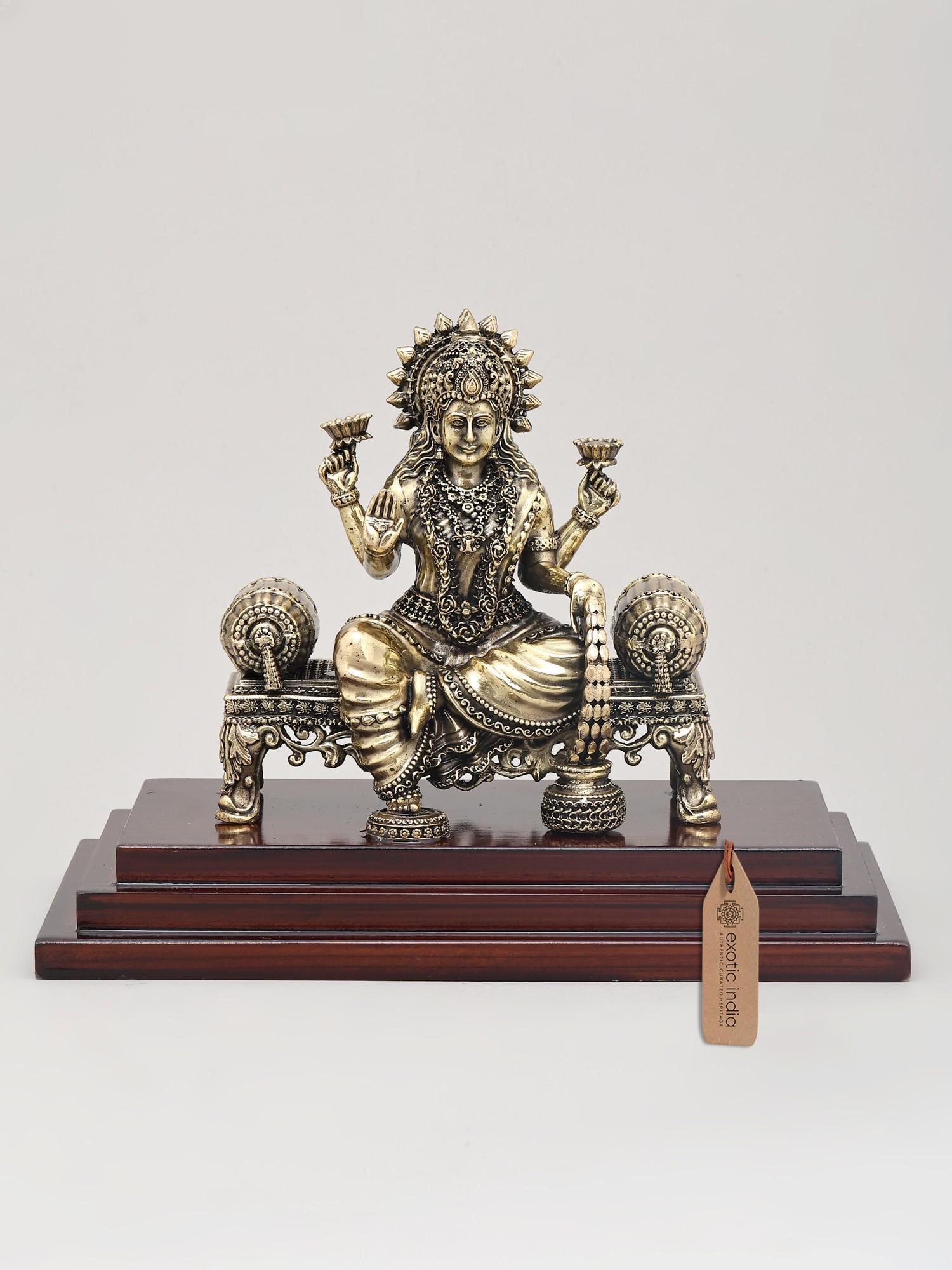 9" Superfine Four Armed Goddess Dhanalakshmi Seated on Asana with Wood Base | Brass Idol: The Divine Embodiment of Prosperity and Fortune Immerse your sacred space in an aura of unparalleled prosperity and divine grace with this exquisite brass idol of Goddess Dhanalakshmi. Seated regally 