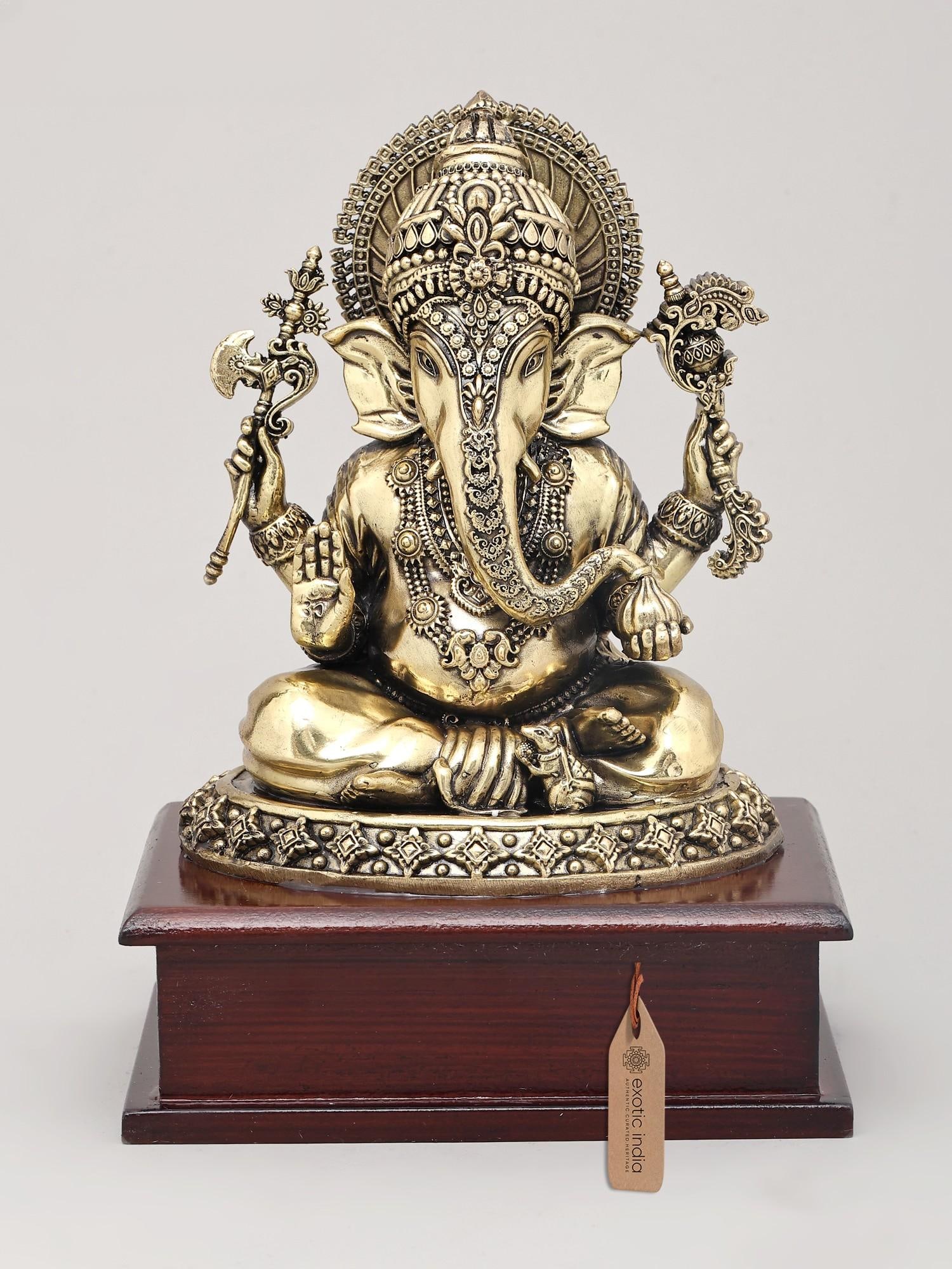 8" Superfine Chaturbhuja Lord Ganapati Holding Modak on Wood Base | Brass Statue: Embodiment of Wisdom and Prosperity Behold this magnificent brass statue, a divine representation of Lord Ganesha in his Chaturbhuja form, seated serenely upon an ornate base. The term "Chaturbhuja" s