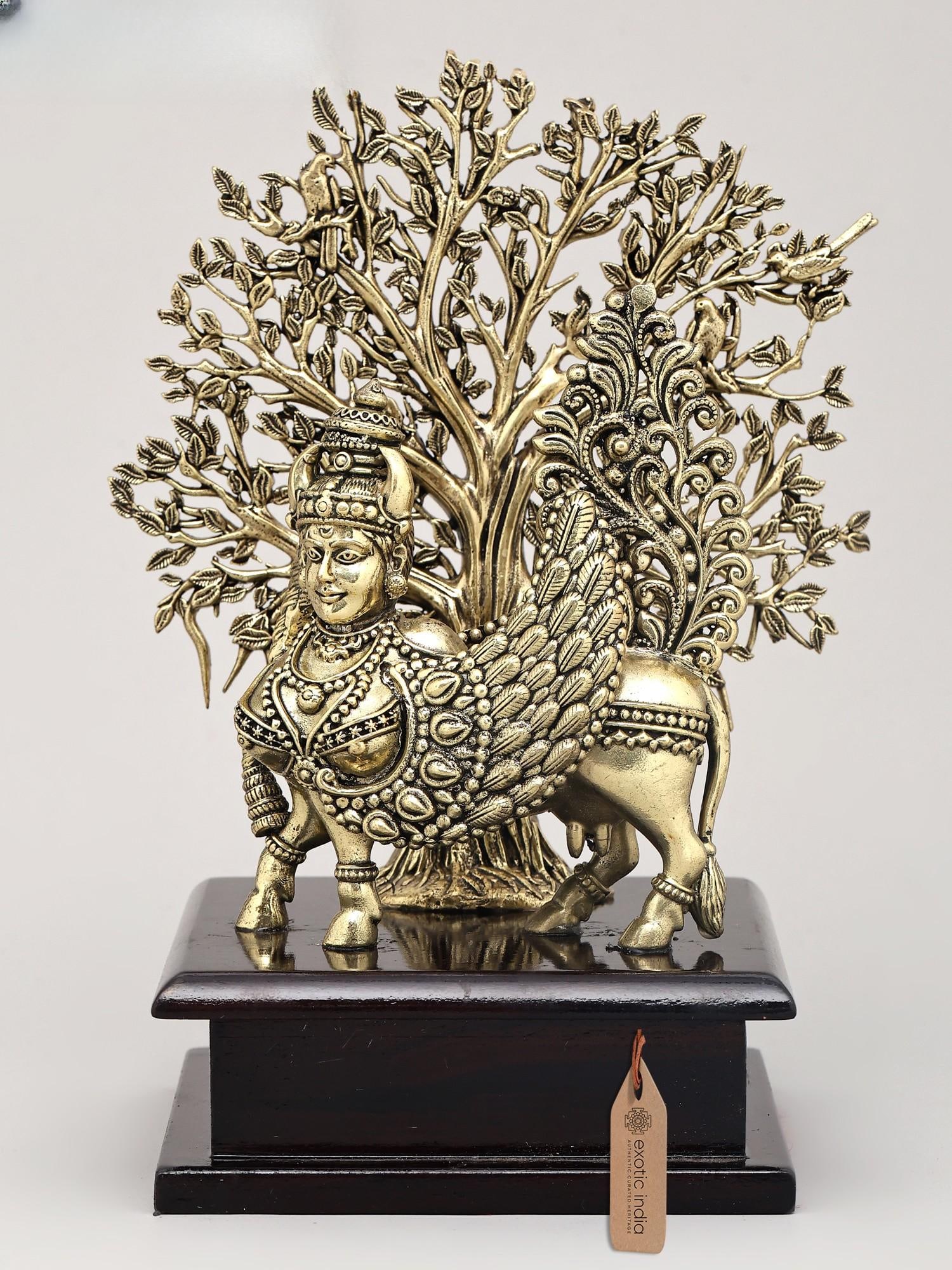 7" Superfine Goddess Kamdhenu Standing with Tree of Life on Wood Base | Brass Statue: The Divine Cow of Plenty This exquisite brass sculpture depicts the celestial cow Kamadhenu, an embodiment of abundance and prosperity, intertwined with the universal symbol of the Tree of Life. Kamad