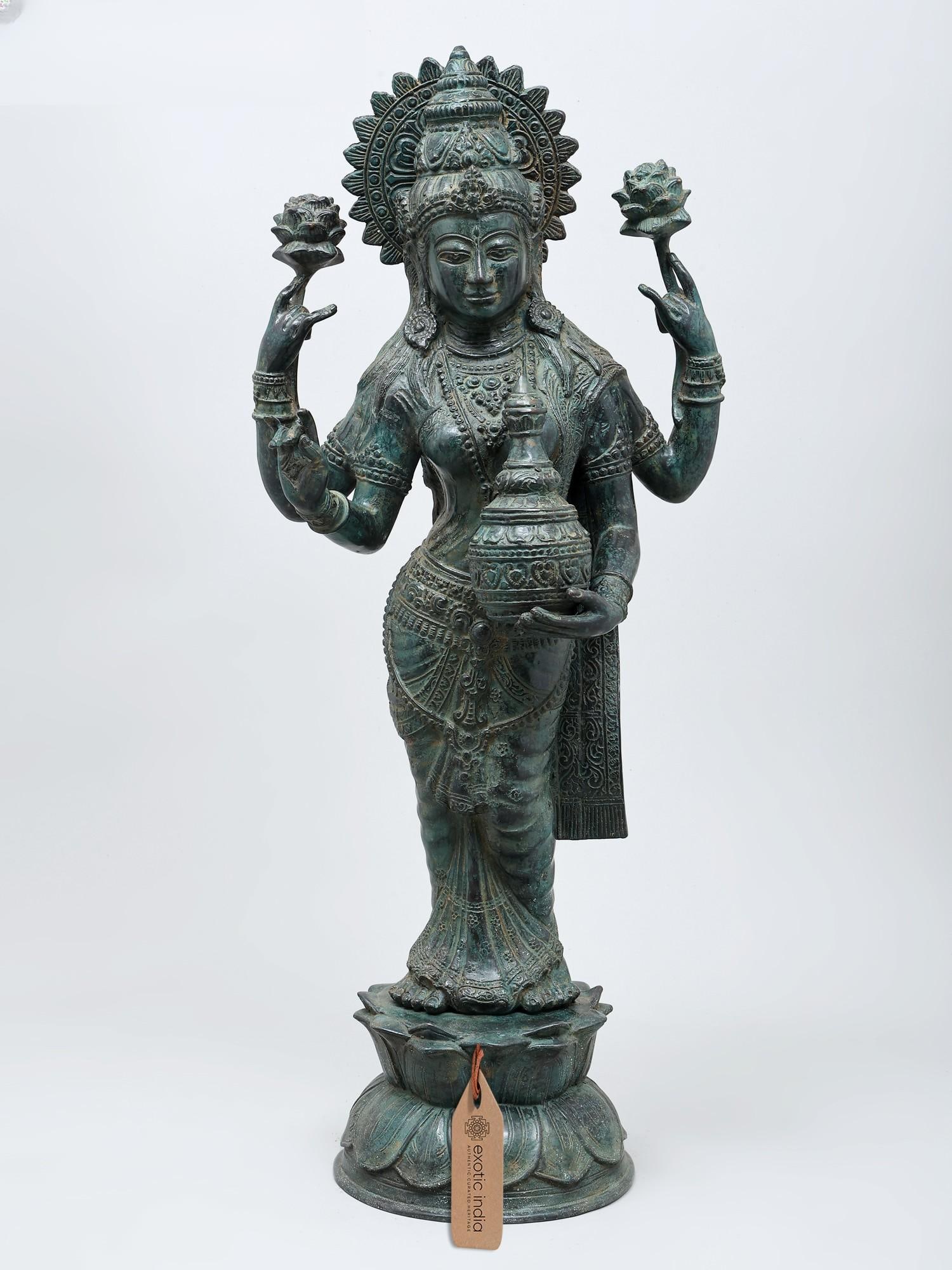 27" Standing Goddess Lakshmi with Wealth Pot | Brass Statue: The Embodiment of Prosperity and Grace This magnificent brass statue captures the divine essence of Goddess Lakshmi, the revered deity of wealth, prosperity, and auspiciousness in Hinduism. Standing t