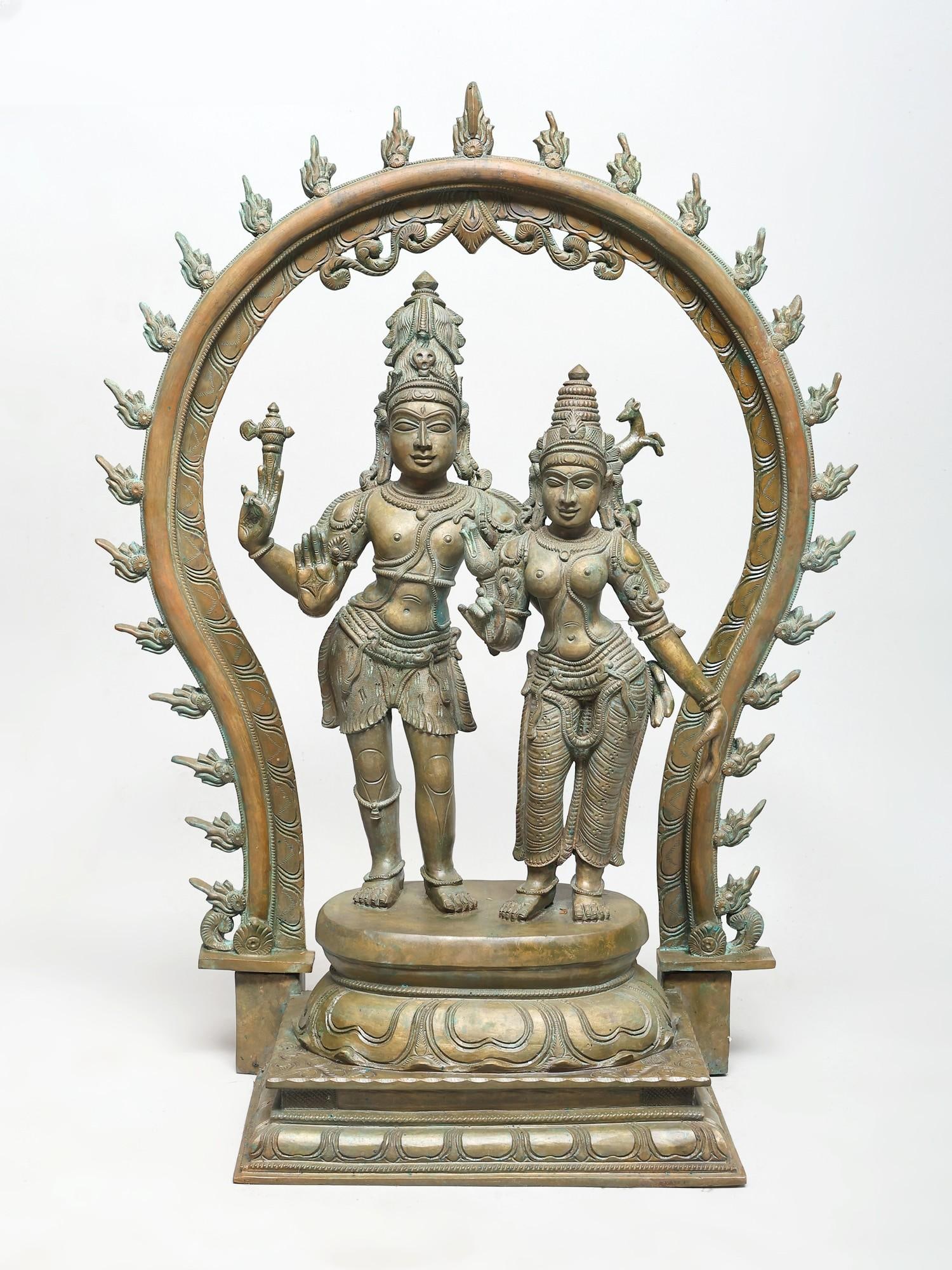 25" Standing Shiva Parvati with Arch | Madhuchista Vidhana (Lost-Wax) | Panchaloha Bronze from: Divine Union and Cosmic Dance This magnificent bronze sculpture captures the eternal union of Lord Shiva and Goddess Parvati, standing as a testament to divine love and cosmic energy. The intricate de