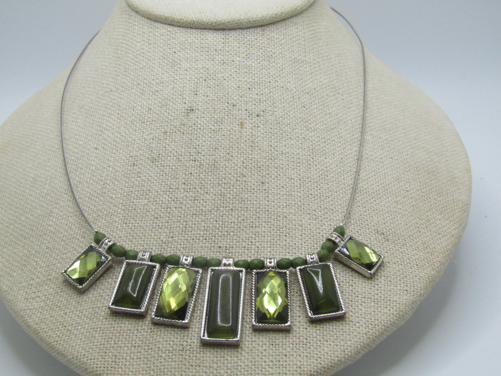 Green Faceted Bib Necklace, 20", Silver Tone: Title: Green Faceted Bib Necklace, 20", Silver Tone Description: Green Faceted Bib Necklace, 20", Silver Tone. The necklace is a coated wire necklace with lobster clasp. It is 17" long with a 3" exten