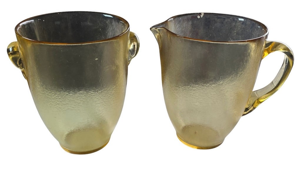 Pair of Amber Glass Pitchers: This lot features a pair of amber-colored glass pitchers, characterized by their textured, possibly crackled or hammered, surface and clear applied handles. Each pitcher also features a spout for