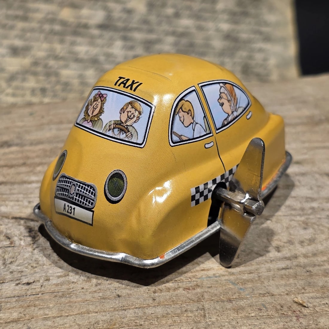 Tin Litho Taxi Toy Wind-Up Mechanical Cab Car: Reproduction Vintage-style tin lithograph taxi toy featuring colorful passenger graphics and a side-mounted wind-up mechanism. Taxi cabs became a familiar part of city life during the early and mid-20