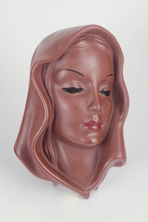 Goldscheider, Austria. Art Deco female portrait wall mask in glazed ceramic. Approx. 1940s.: Goldscheider, wall mask. Art Deco wall mask in glazed ceramic, model 7831, formed as a stylised female portrait with a draped veil-like surround. Glaze in a deep burgundy tone. Retains the original Go