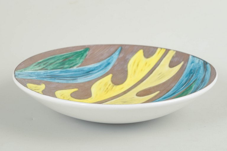 Mari Simmulson for Upsala Ekeby, Sweden. Round faience bowl with a stylised agave leaf motif in: Mari Simmulson for Upsala Ekeby, "Agave" bowl. Decorative round bowl in glazed faience with a stylised agave leaf motif in yellow, blue, and green tones against a ribbed brown ground. The relief