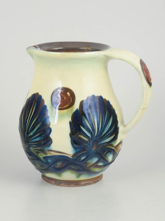 Kahler, Denmark. Stoneware jug with relief leaf and band motifs decoration. Approx. 1930s.: Kahler, jug with relief decoration. Jug in glazed stoneware with pronounced relief decoration featuring stylised leaf and band motifs in blue and green tones against a light ground glaze. The form is 