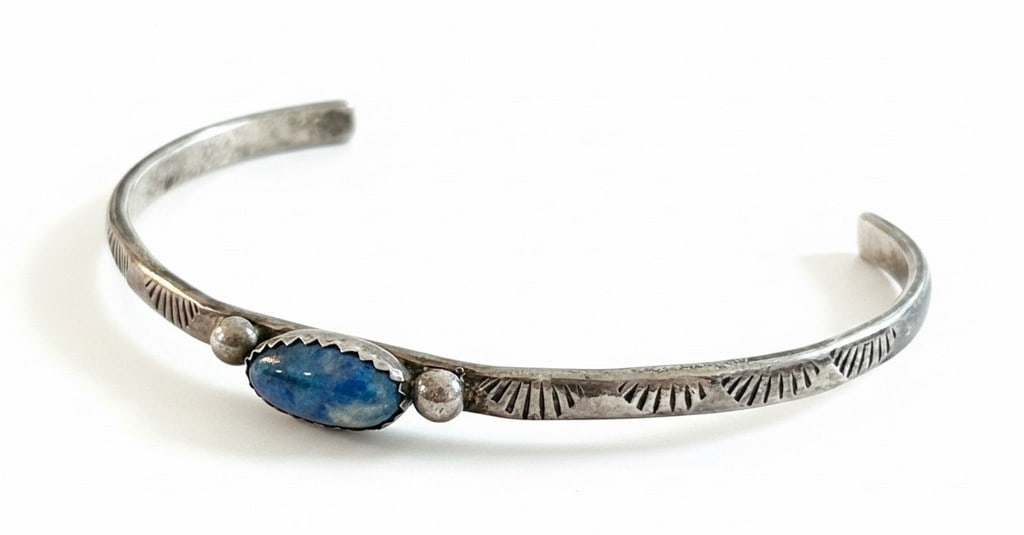 Native American Sterling Silver and Lapis Lazuli Cuff Bracelet: A handcrafted sterling silver cuff bracelet, likely Native American in origin, featuring a central oval lapis lazuli cabochon flanked by two silver spheres. The silver band is adorned with stamped