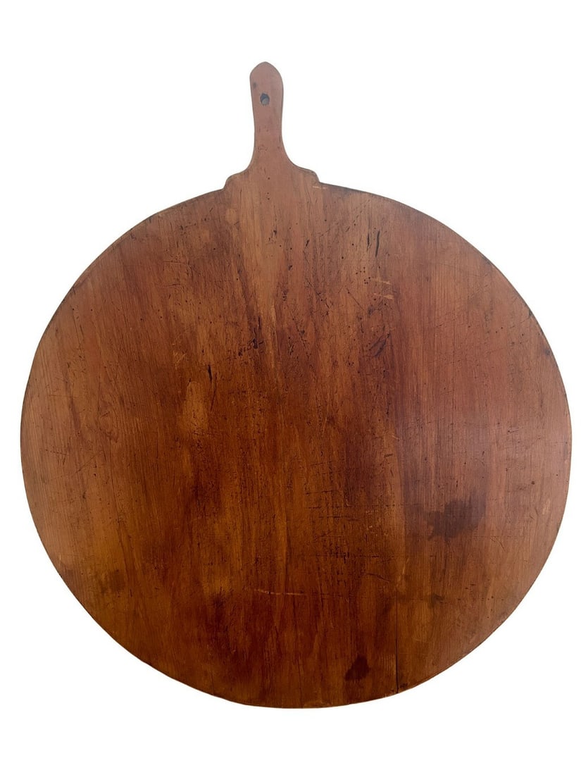 Large Antique French Dough Board with Handle: This large antique French dough board, likely dating from the 19th century, is crafted from a single piece of deeply aged wood. Its round form with an integrated handle and a hanging hole suggests
