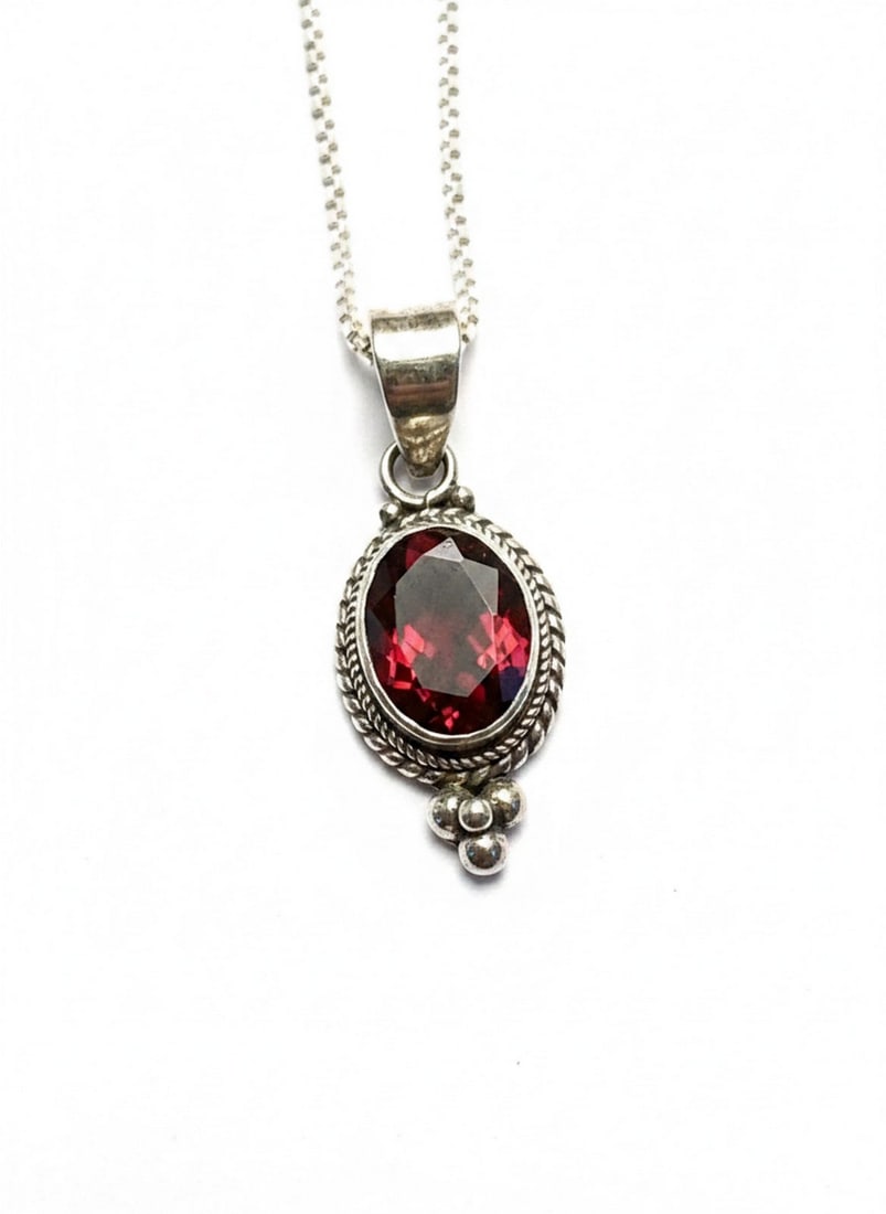 Sterling Silver and Garnet Pendant Necklace: A sterling silver pendant featuring an oval-cut garnet stone, set in a decorative bezel with twisted rope detailing and three silver spheres at the base. The pendant is suspended from a sterling