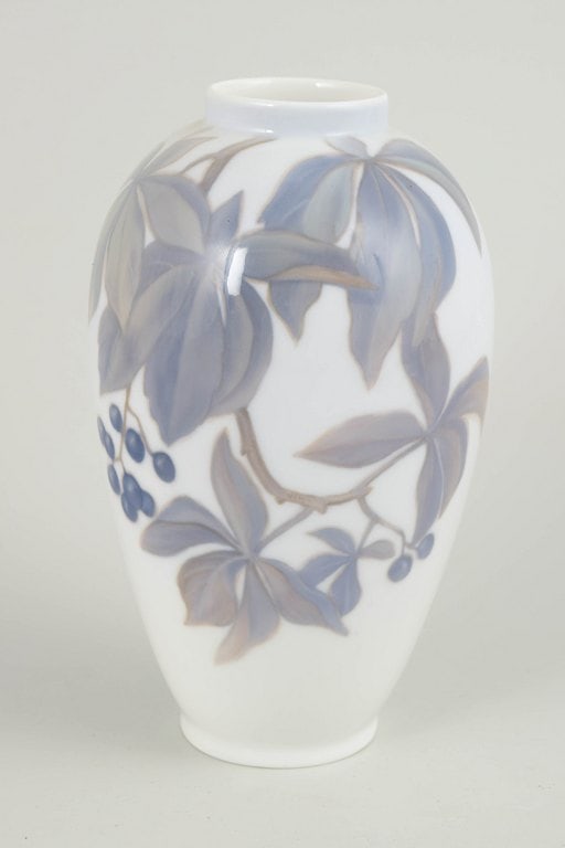 Royal Copenhagen, Denmark. Slender baluster-shaped porcelain vase decorated with leaves and berries: Royal Copenhagen, vase. Slender baluster-shaped porcelain vase with a hand-painted underglaze decoration of stylised leaves and berries in muted blue-grey and brownish tones on a white ground. The