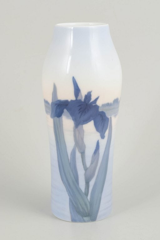 Royal Copenhagen, Denmark. Tall porcelain vase decorated with floral motifs. Approx. 1920s.: Royal Copenhagen, vase. Tall, subtly faceted porcelain vase with a hand-painted underglaze decoration of iris flowers in deep blue tones with green stems, set against a light, softly toned ground. The