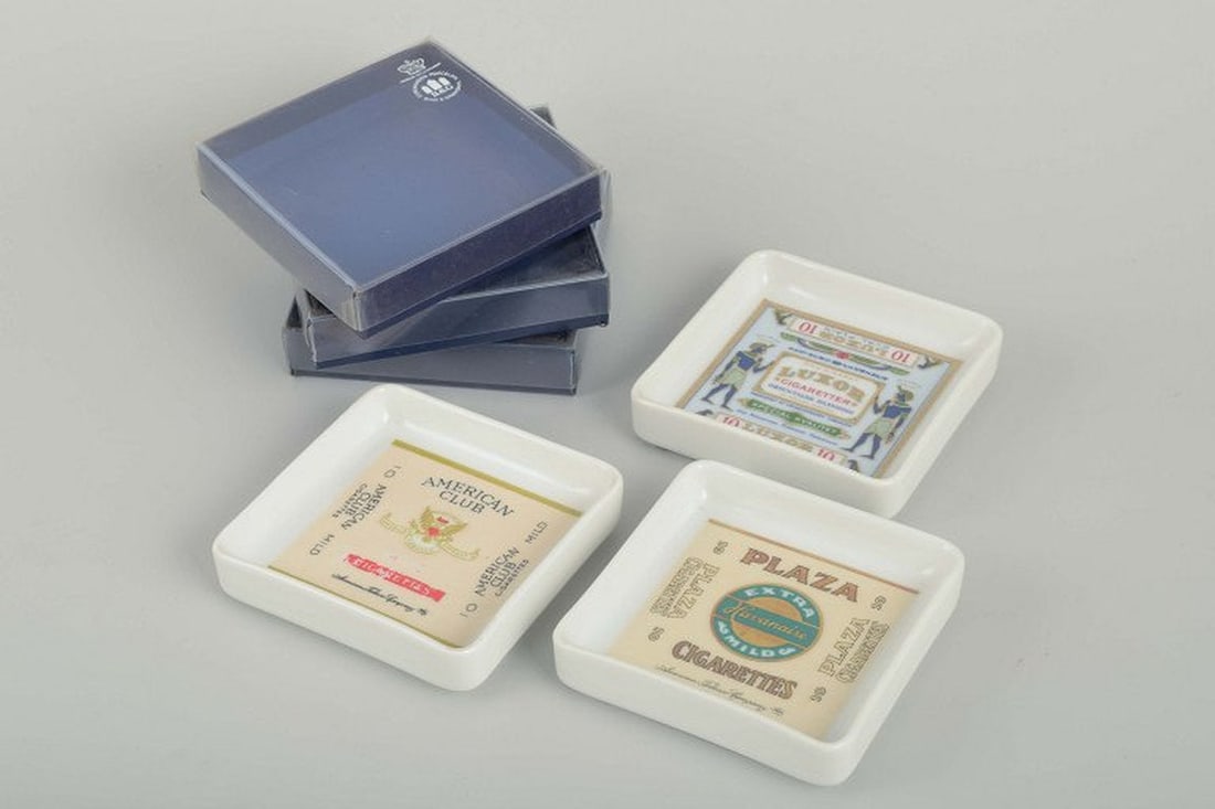 Bing & Grøndahl, Denmark. Set of three square porcelain ashtrays. 1980s.: Bing & Grøndahl Ashtrays, 1980s. Set of three square porcelain ashtrays, each decorated with classic tobacco and cigar motifs. Supplied in original boxes. Origin: Denmark. Designer/Manufacturer: Bing