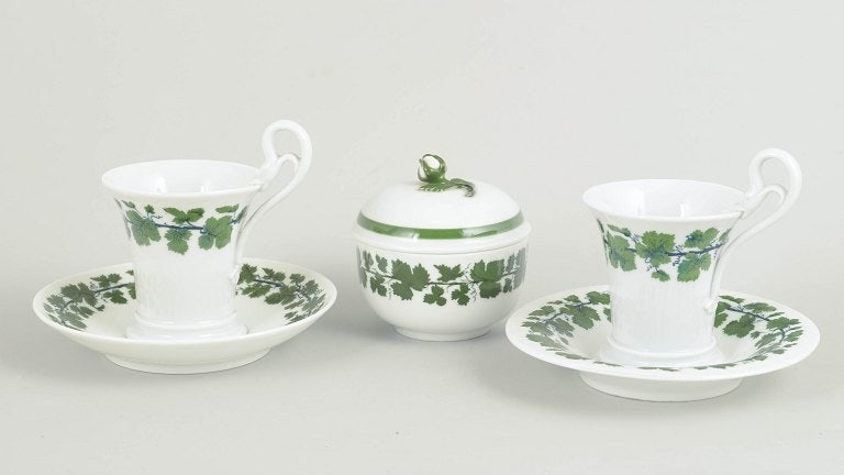 Meissen, Germany. Pair of porcelain coffee cups with saucers and sugar bowl with a green vine leaf: Meissen, Vine Leaves, coffee cups with saucers and sugar bowl. A pair of porcelain coffee cups with swan handles and matching saucers, accompanied by a sugar bowl, decorated with a green vine leaf bor