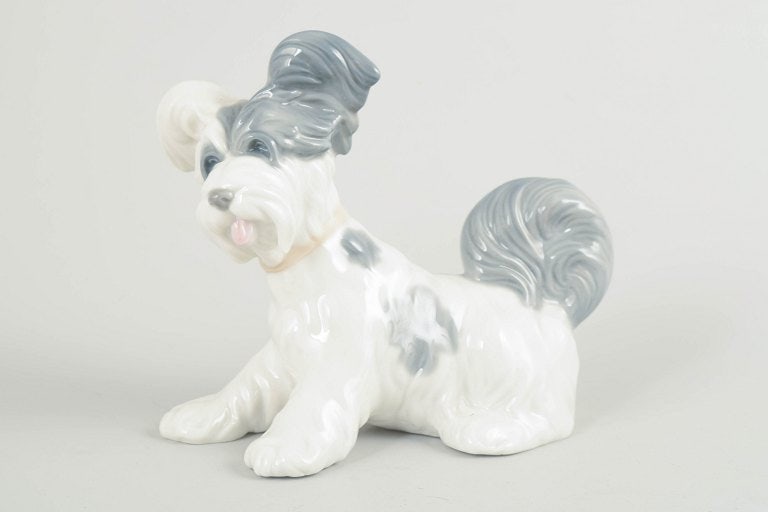 Lladró, Spain. Porcelain dog figurine in white glaze with grey and pale blue details. Approx.: Lladró, Spain, dog figurine. Naturalistic porcelain figurine depicting a small seated dog, modelled in white glaze with grey and pale blue details. Smooth, glossy surface and softly rounded forms, ch