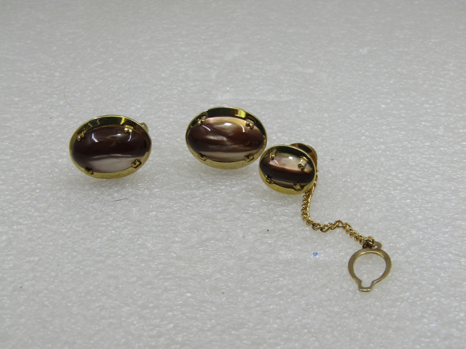 Vintage Brown Cateye Cufflinks and Tie Tack Set, 1960's: Vintage Brown Cateye Cuff Links & Tie Tack Set, 1960's. The cuff links are oval and appx. 1" by 3/4" in the setting and the tie tack with chain are appx. 5/8" long by 1/2" wide. Gold Tone. They are si