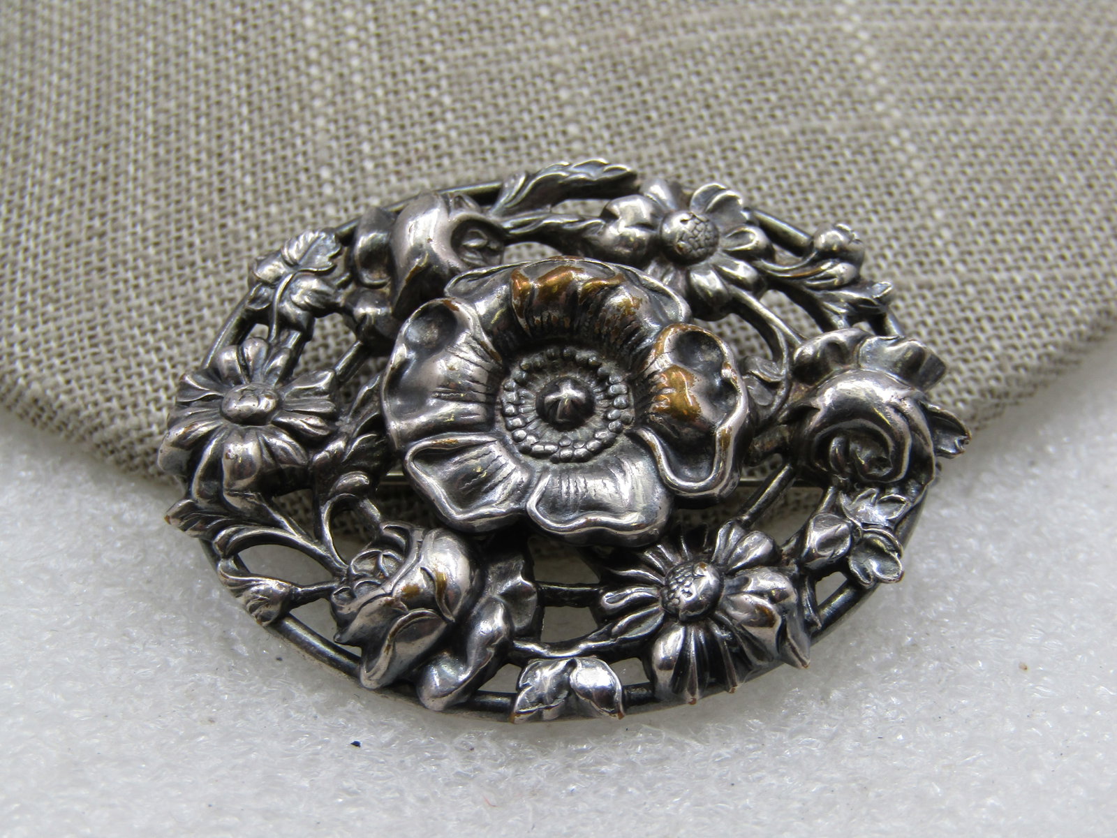 Vintage Silver Plated Mixed Floral Brooch, Mid-Century: , 1-7/8" wide and 1.5" tall. Repousse large blossom in the center with flowers such as roses, daisies around the outer edge with open area between the flowers. Oval brooch, locking clasp.