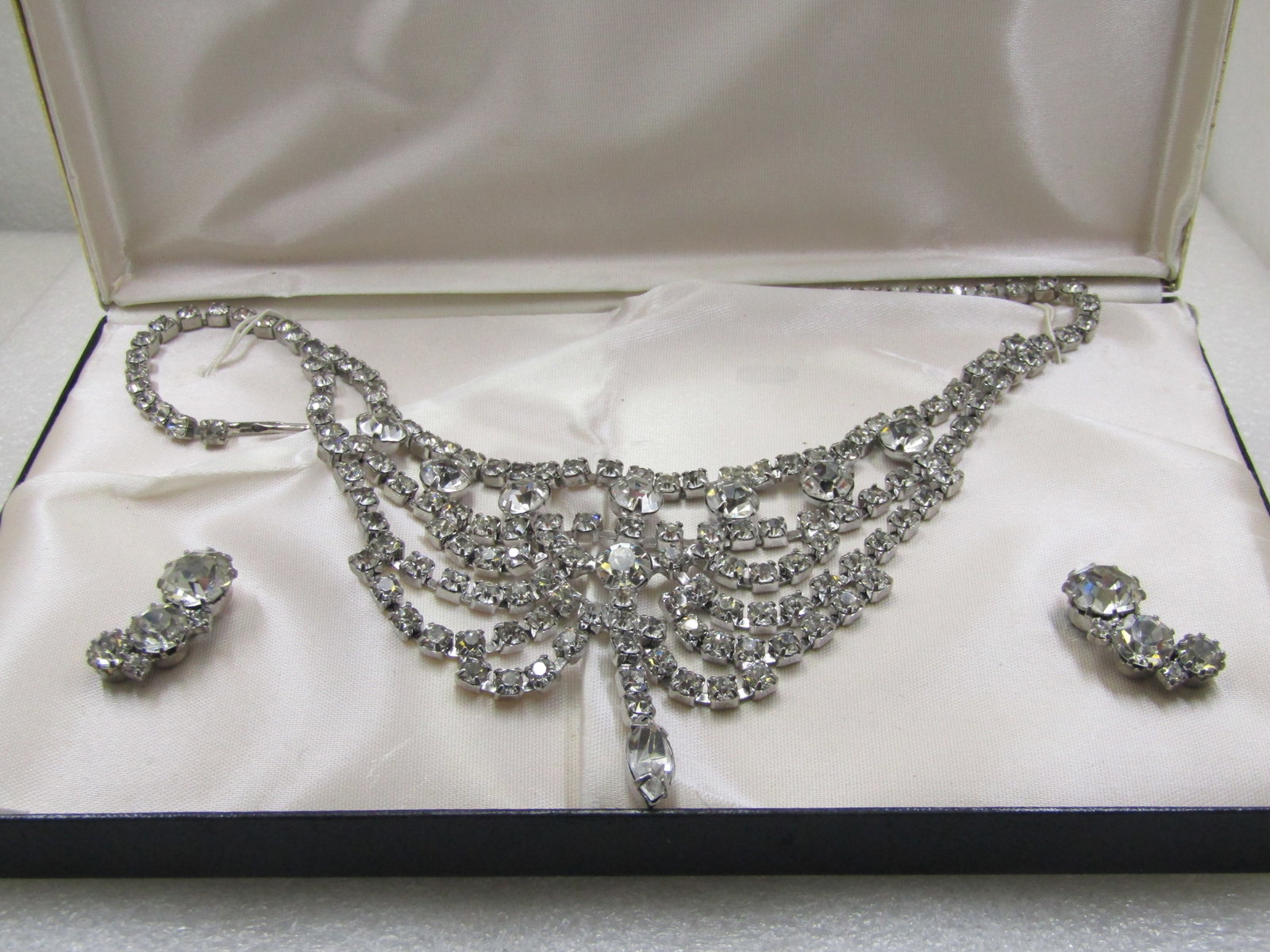 Vintage Rhinestone Bib Necklace and Earrings Art Deco Themed Set in Box: Vintage Rhinestone Bib Necklace & Earrings Art Deco Themed Set in Box. The necklace has a hook clasp and is 16" wide with the center having a 2 3/4" drop with a swag bib and a mis of round stones in d