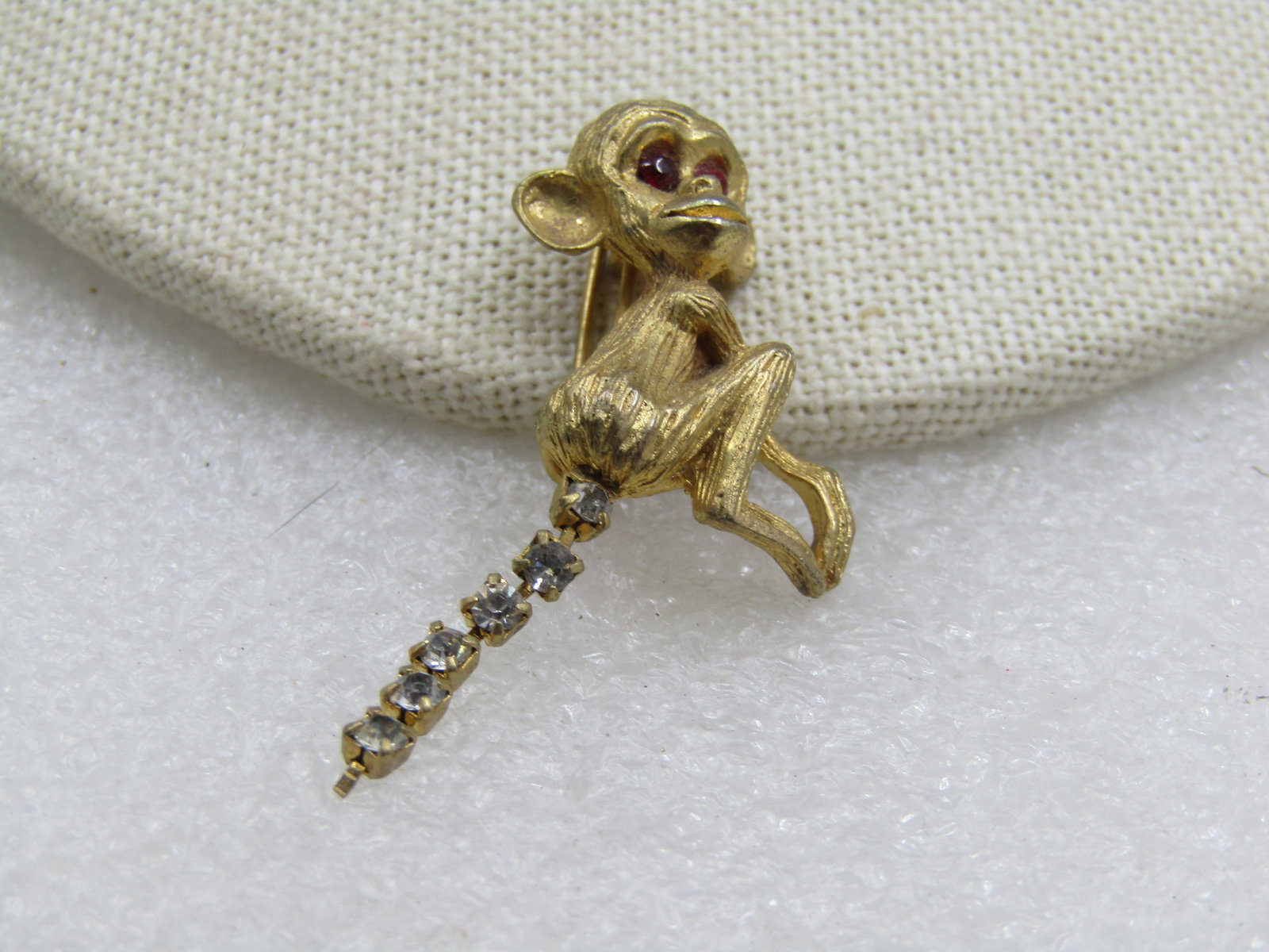 Vintage Monkey With Rhinestone Tail Brooch, 1950's-1960's: Vintage Monkey With Rhinestone Tail Brooch, 1950's-1960's. Red rhinestone deep set eyes and a tailw ith 6 rhinestones in a chain. C clasp. Textured gold tone finish. Not signed by the maker. Very good
