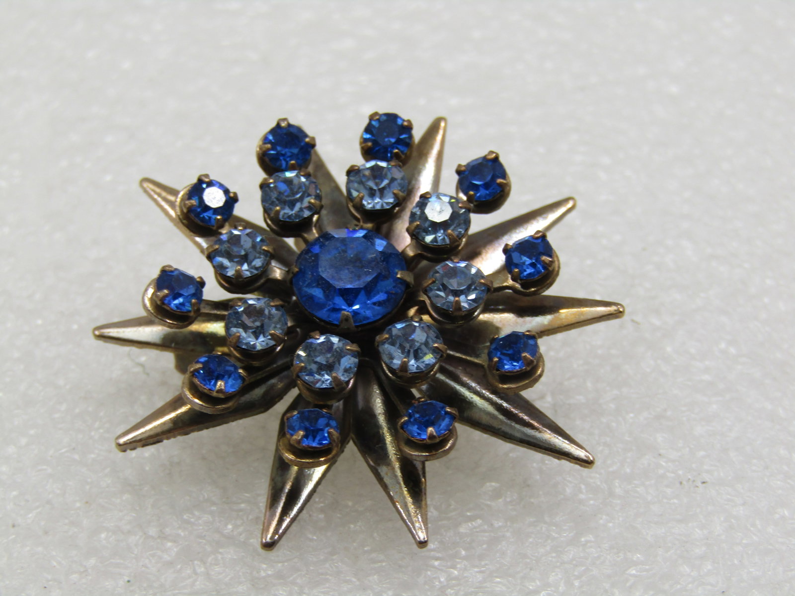 Vintage Shades of Blue Rhinestone Starburst Brooch, 1-5/8": Vintage Shades of Blue Rhinestone Star Brooch, 1-5/8", 1950's. Silver tone on the back of the setting and gold tone on top, with pointed lower tier creating the starburst and above that are three leve