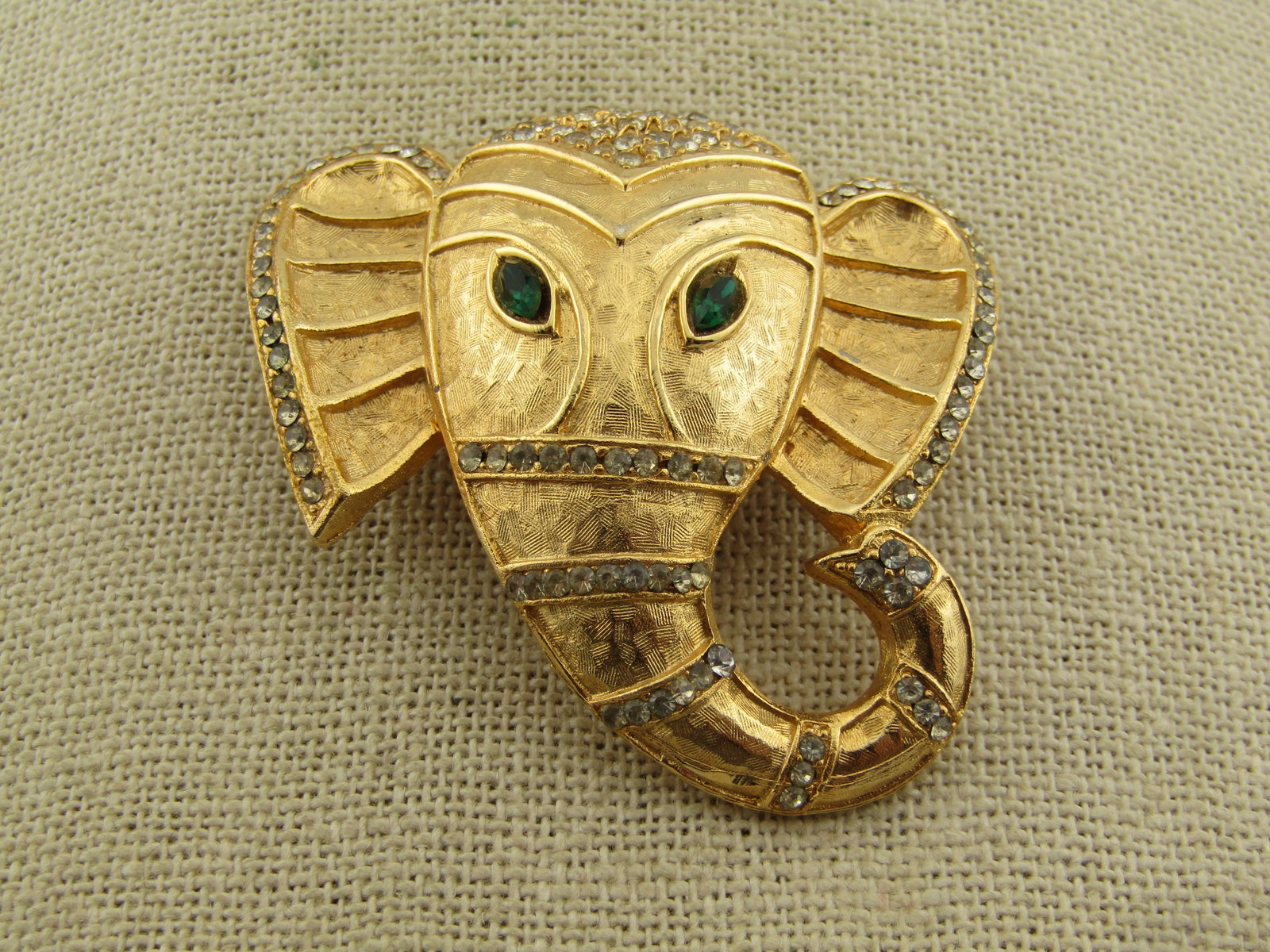 Vintage Gold Tone India Elephant Brooch, Rhinestones, 1970's-1980's: Vintage Gold Tone India Elephant Brooch, Rhinestones, 1970's-1980's. This has a textured finish with raised details and clear rhinestones decorating the brooch on the forehead, trunk and ear edges.