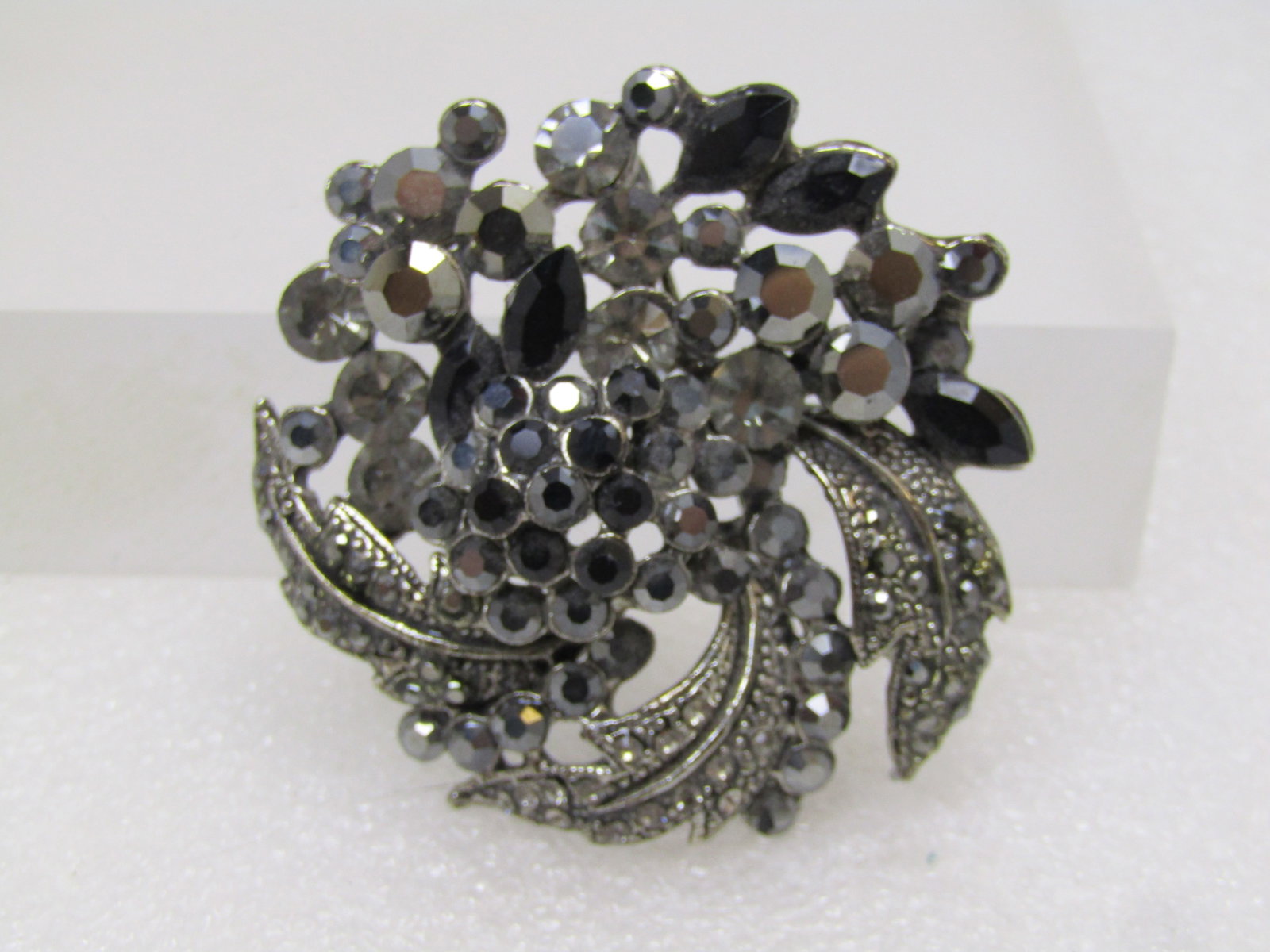 Black and Gray Rhinestone Floral Brooch, Silver and Black Tone Metal, 1980's-1990's: Black and Gray Rhinestone Floral Brooch, Silver and Black Tone Metal, 1980's-1990's. This has a blossom design with raised black stones in the center and silver tone curved leaves with black and gray